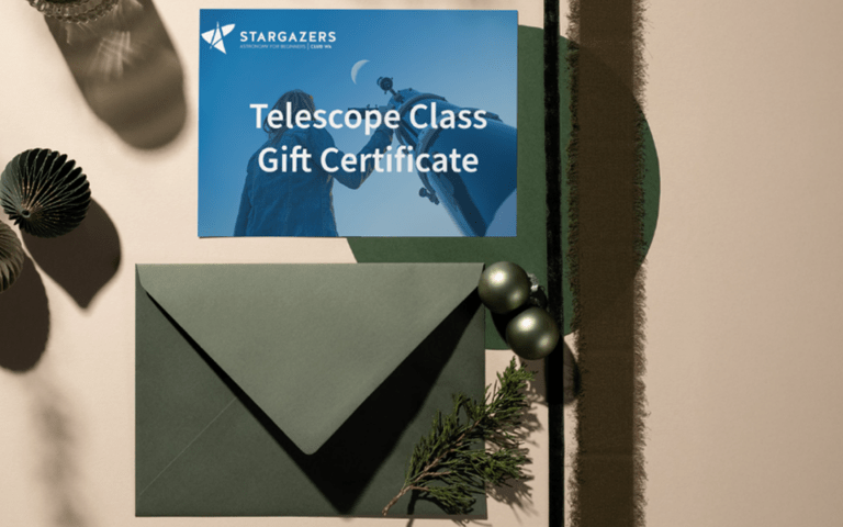 A Stargazers Club WA telescope class gift certificate sits on a table with an envelope and some shells