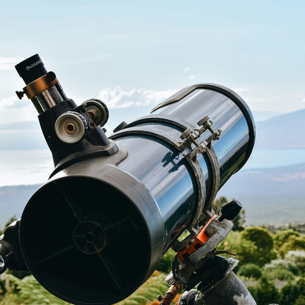 A shiny telescope looks at distant scenery during daylight. Practicing using your telescope during the day is one of our tips.