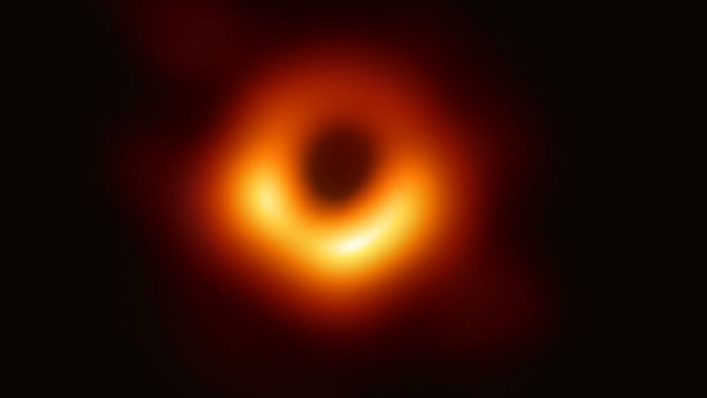 The first image of a black hole, seen as a bright circular disc, glowing orange and yellow, with a dark centre