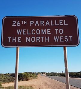 Image shows a brown sign reading "26th parallel welcome to the north west"